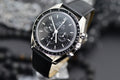 Omega Speedmaster Professional Moonwatch black chronograph dial with tachymeter bezel, three-quarter angled view on black leather strap