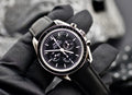 Omega Speedmaster Professional Moonwatch held in a gloved hand, showing black dial, tachymeter bezel, and stainless steel case