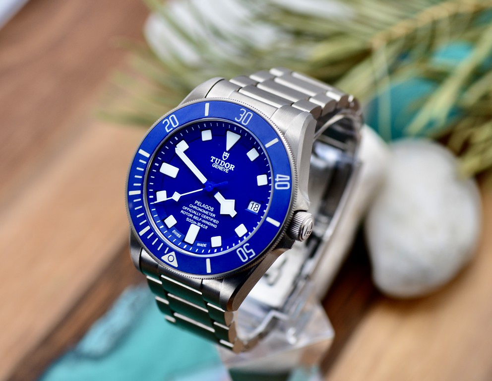 Tudor Pelagos 42 blue dial and titanium bracelet, styled lifestyle shot on wood surface with greenery