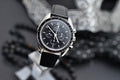 Omega Speedmaster Professional Moonwatch black dial and stainless steel case on black leather strap, styled flat lay shot