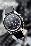 Omega Speedmaster Professional Moonwatch black dial and tachymeter bezel close-up, angled portrait shot on black leather strap