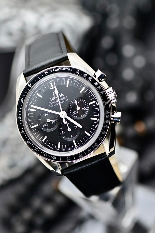 Omega Speedmaster Professional Moonwatch black dial and tachymeter bezel close-up, angled portrait shot on black leather strap