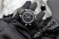 Omega Speedmaster Professional Moonwatch held in hand, displaying black dial, tachymeter bezel, and black leather strap